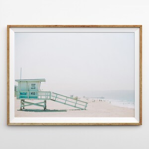 May include: A framed photograph of a lifeguard stand on a beach. The stand is painted light blue and white and has a number "40" on the side. The beach is sandy and there are people in the distance.