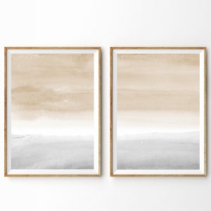 May include: Two framed watercolor paintings with a gradient of beige and gray. The paintings are in simple wooden frames and are hung on a white wall.