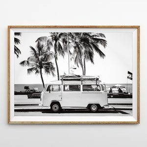 May include: Black and white photograph of a vintage white van parked on a street with palm trees in the background. The van has a surfboard and other luggage strapped to the roof.