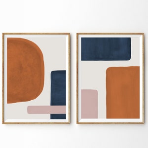 Op de afbeelding: Twee ingelijste abstracte kunstprints met geometrische vormen in tinten oranje, bruin, roze en blauw.