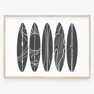 May include: A black and white print of five surfboards with different designs, including a sun, waves, and a line pattern. The surfboards are framed in a light wood frame.
