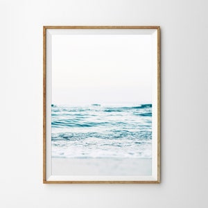 Peut inclure: Une photographie encadr&eacute;e d'un oc&eacute;an bleu avec des vagues blanches et mousseuses qui se brisent sur le rivage. Le ciel est bleu clair et l'eau est claire et calme.