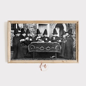 May include: A black and white photograph of a group of women dressed as witches, sitting around a table with teacups and a teapot. They are wearing black cloaks and pointed hats.