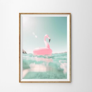 May include: A pink flamingo inflatable pool float in a turquoise blue body of water. The water is clear and you can see the bottom of the pool. The sky is a light blue.