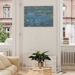 May include: A framed print of a painting depicting a pond with water lilies and a blue sky. The painting is in a light wood frame and is hanging on a white wall.