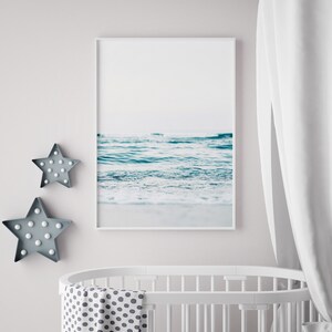 Peut inclure: Un lit b&eacute;b&eacute; blanc avec une couverture blanche et grise &agrave; pois. Une photographie encadr&eacute;e d'un oc&eacute;an bleu avec des vagues blanches est accroch&eacute;e au mur au-dessus du lit b&eacute;b&eacute;. Deux lumi&egrave;res en forme d'&eacute;toile grises sont sur le mur &agrave; gauche du lit b&eacute;b&eacute;.