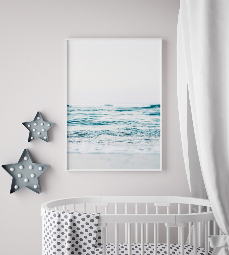 Peut inclure: Un lit b&eacute;b&eacute; blanc avec une couverture blanche et grise &agrave; pois. Une photographie encadr&eacute;e d'un oc&eacute;an bleu avec des vagues blanches est accroch&eacute;e au mur au-dessus du lit b&eacute;b&eacute;. Deux lumi&egrave;res en forme d'&eacute;toile grises sont sur le mur &agrave; gauche du lit b&eacute;b&eacute;.