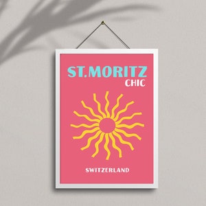 May include: A pink and white framed poster with the text "ST. MORITZ CHIC" in blue and yellow. The poster features a yellow sun with wavy rays on a pink background. The text "SWITZERLAND" is at the bottom of the poster.