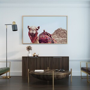 May include: A living room interior with two dark green leather chairs, a dark wood cabinet, a round wooden coffee table with a gold metal base, and a framed print of a camel in front of a pyramid.