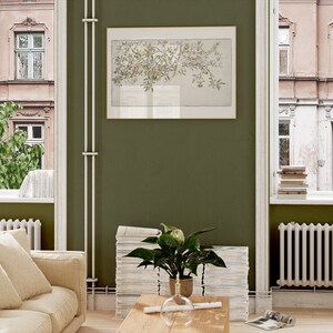 May include: A living room interior with a green wall, a white couch with beige pillows, a stack of magazines, a potted plant, a wooden coffee table, and a framed print of a tree branch.