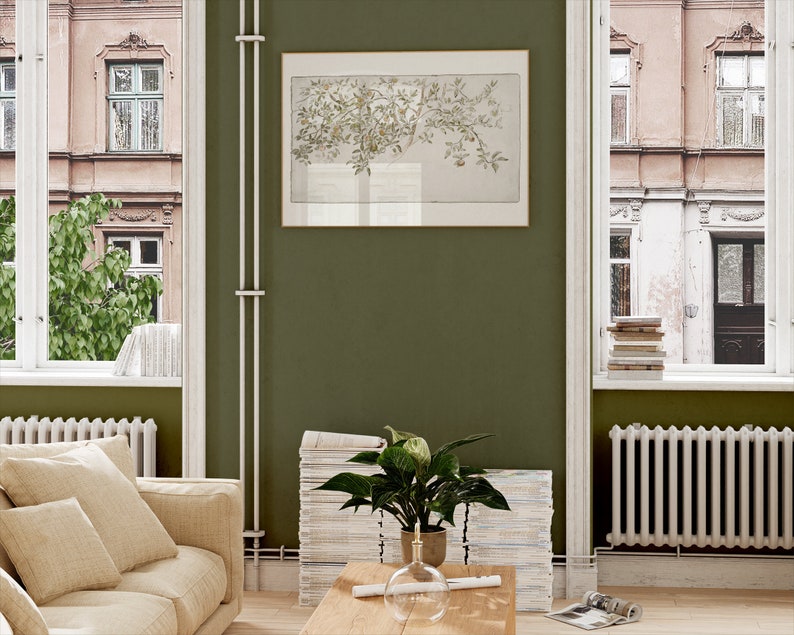 May include: A living room interior with a green wall, a white couch with beige pillows, a stack of magazines, a potted plant, a wooden coffee table, and a framed print of a tree branch.