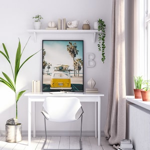 May include: A white desk with a white chair and a framed print of a yellow vintage van with surfboards on top, parked on a beach with palm trees in the background.