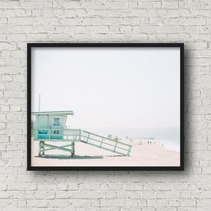 May include: A light blue lifeguard stand with a white roof and a sign that reads "Lifeguard Station 40 Keep Out". The stand is on a sandy beach with a pier in the distance.