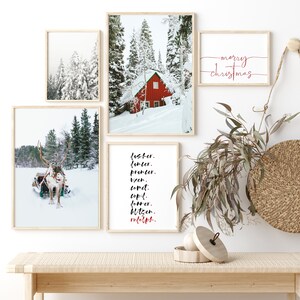 Op de afbeelding: Een set van vijf ingelijste prints met een winterthema. De prints tonen een rode hut in een besneeuwd bos, een rendier dat een slee trekt en een lijst met rendiernamen. De prints zijn gerangschikt op een witte muur met een houten bank eronder. De tekst op de prints luidt "Jester, Dancer, Prancer, Vixen, Comet, Cupid, Donner, Blitzen, Rudolph" en "merry christmas".