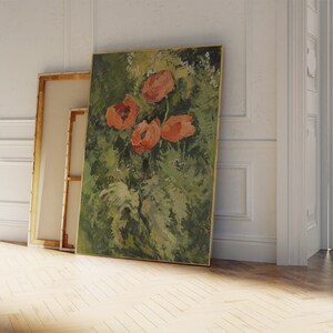 Puede incluir: Una pintura al &oacute;leo de flores naranjas sobre un fondo verde, enmarcada en oro. Otros dos lienzos se apoyan en la pared. La pintura se exhibe en una habitaci&oacute;n con paredes blancas y suelo de madera.