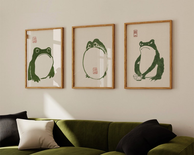 May include: Three framed prints of green frogs on a white background. The frogs are in different poses, one is sitting, one is standing, and one is in a circle. The frames are light brown wood.