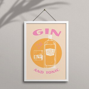 May include: A white framed poster with a peach background and a yellow circle. The circle contains a line drawing of a bottle of gin and a glass of gin with ice. The text "GIN AND TONIC" is in white letters below the circle. The word "GIN" is in pink letters above the circle.