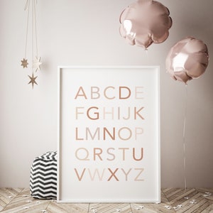 May include: A white framed poster with the alphabet in brown, pink, and beige letters on a white background. The poster is hanging on a white wall with two pink balloons and a wooden star mobile hanging above it.