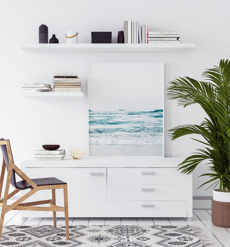 Peut inclure: Une commode blanche avec trois tiroirs et une photographie encadr&eacute;e d'une sc&egrave;ne de plage au-dessus. Un palmier en pot se trouve &agrave; droite de l'image. Une chaise en bois avec un si&egrave;ge noir est au premier plan.