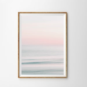 May include: A framed abstract photograph of a blurred ocean scene with a pink and blue color scheme. The image is in a light wood frame.