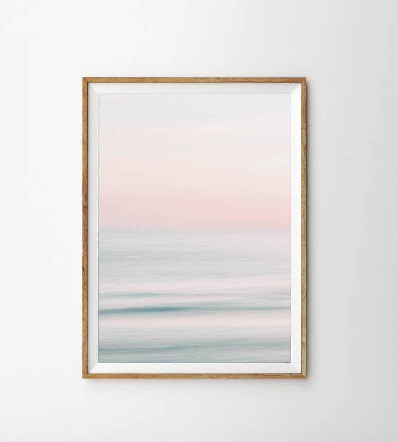 May include: A framed abstract photograph of a blurred ocean scene with a pink and blue color scheme. The image is in a light wood frame.