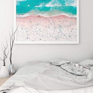 Op de afbeelding: Een luchtfoto van een strand met turquoise water en wit zand. Het strand is druk met mensen en de schaduwen van palmbomen zijn zichtbaar op het zand.