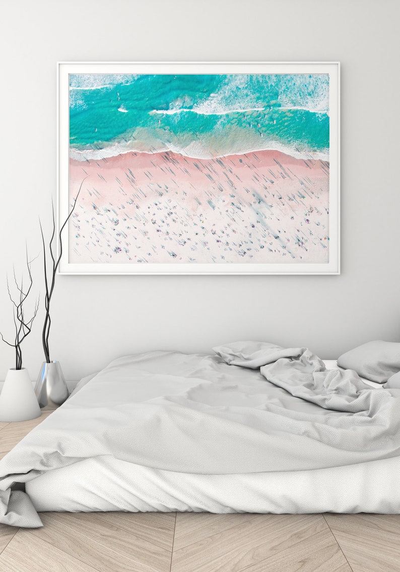 Op de afbeelding: Een luchtfoto van een strand met turquoise water en wit zand. Het strand is druk met mensen en de schaduwen van palmbomen zijn zichtbaar op het zand.