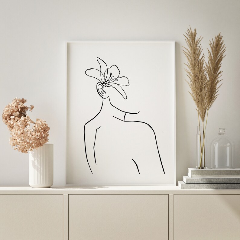 May include: A black and white line drawing of a person with a flower on their head. The drawing is on a white background and is framed in a white frame.