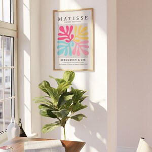 Pode incluir: Uma impress&atilde;o emoldurada de uma obra de arte de Matisse intitulada "Papiers Decoupes" que apresenta formas abstratas em rosa, amarelo e azul. A impress&atilde;o est&aacute; em uma moldura de madeira e tem o texto "BERGGRUEN & CIE" e "Du Vendredi 27 Fevrier au Samedi 28 Mars 1953" na parte inferior.