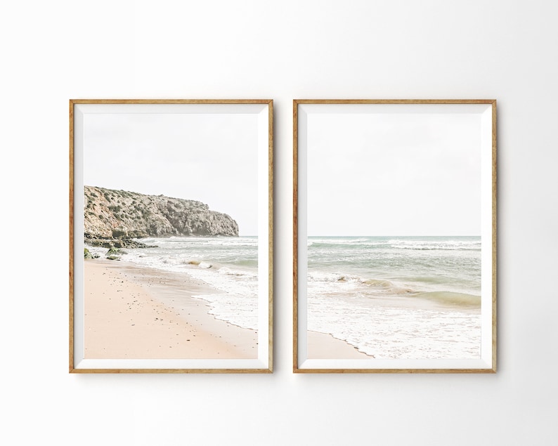 May include: Two framed beach prints. One print shows a sandy beach with a rocky cliffside. The other print shows the ocean with waves. Both prints have a white border and a gold-colored frame.