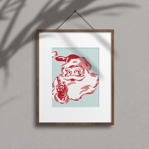 May include: A framed print of a vintage illustration of Santa Claus with a red hat and beard, against a light blue background. He is smiling and pointing with his index finger.