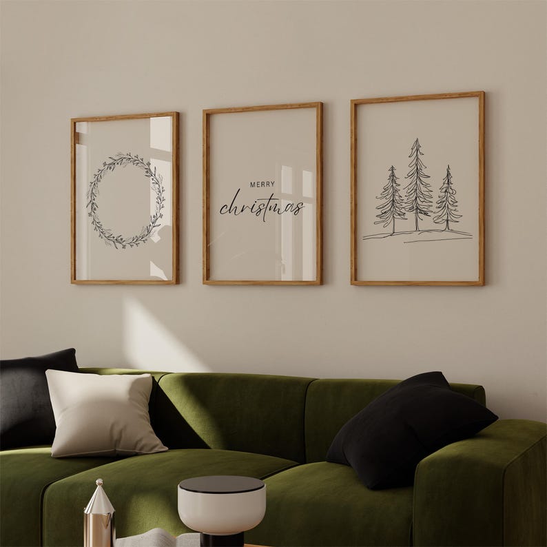 May include: Three framed prints with a minimalist Christmas theme. The left print features a wreath of leaves and berries. The center print says "Merry Christmas" in a simple script font. The right print shows three stylized pine trees.
