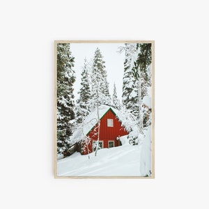 Op de afbeelding: Een rode hut met een groen dak ligt verscholen in een besneeuwd bos. De bomen zijn bedekt met sneeuw en de grond is bedekt met een dikke laag witte sneeuw.
