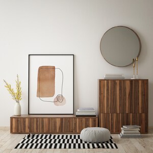 Op de afbeelding: Een houten kast met twee deuren en een plank, een ronde spiegel, een ingelijst abstract print met bruine en roze vormen, een vaas met gele bloemen en een tapijt met een zwart-wit geruit patroon.