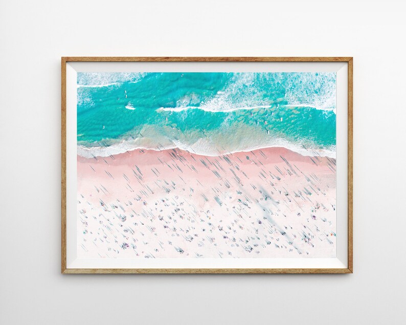 Op de afbeelding: Een luchtfoto van een strand met turquoise water en wit zand. Het strand is vol met mensen en hun schaduwen vallen op het zand.
