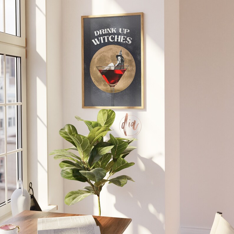 K&ouml;nnte beinhalten: Ein gerahmter Druck mit schwarzem Hintergrund und goldenem Rahmen. Der Druck zeigt eine Hexe, die in einem Martini-Glas sitzt, mit dem Text "Drink Up Witches" dar&uuml;ber.