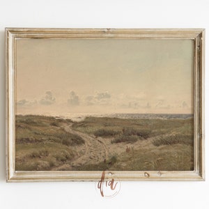 May include: A framed painting of a seascape with a sandy path leading to the ocean. The painting is in a light wood frame with a distressed finish. The sky is a soft blue with white clouds. The ocean is a light blue with whitecaps. The sand is a light brown with green grass.