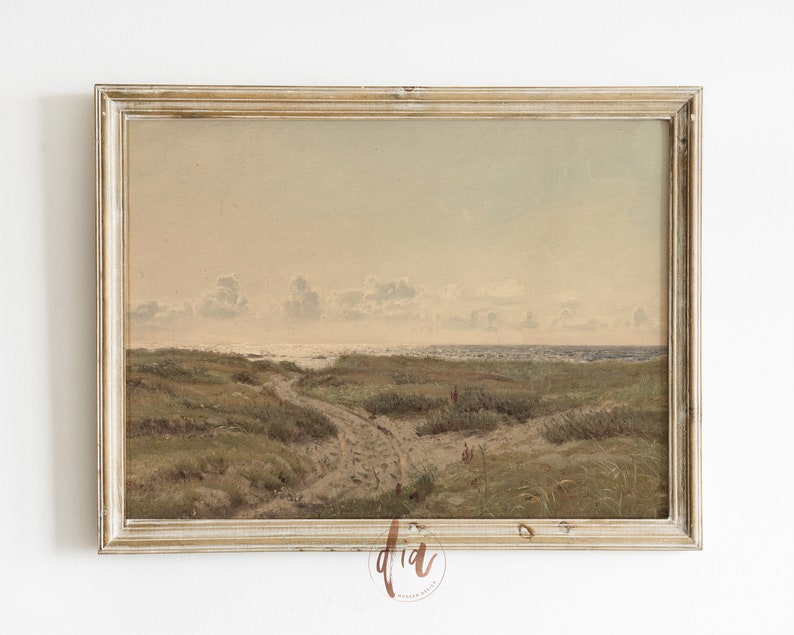 May include: A framed painting of a seascape with a sandy path leading to the ocean. The painting is in a light wood frame with a distressed finish. The sky is a soft blue with white clouds. The ocean is a light blue with whitecaps. The sand is a light brown with green grass.