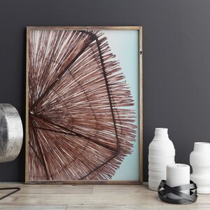 May include: A framed print of a brown woven beach umbrella against a blue sky. The print is on a table with a silver lamp, two white vases, a white candle, and a black metal candle holder.