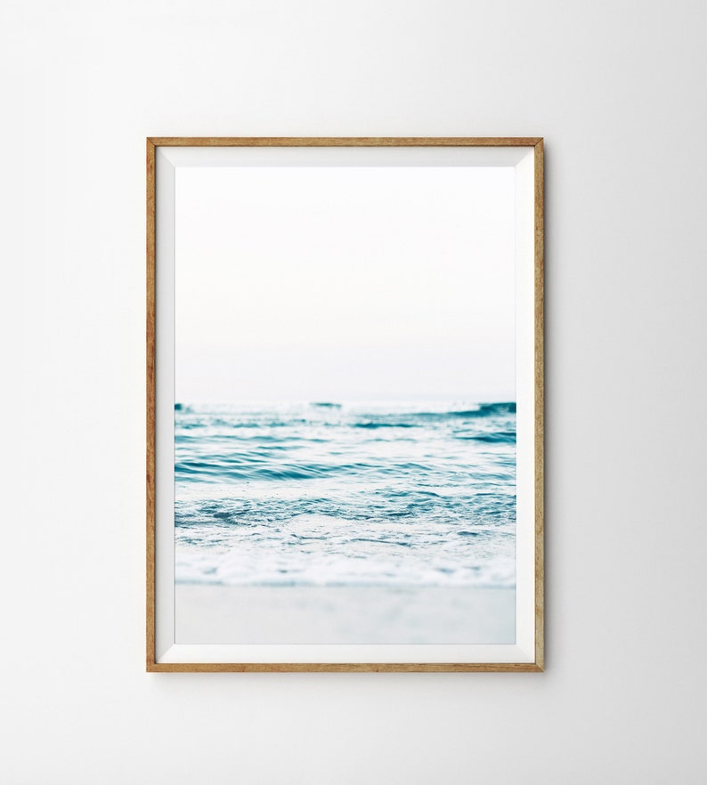 Peut inclure: Une photographie encadr&eacute;e d'un oc&eacute;an bleu avec des vagues blanches et mousseuses qui se brisent sur le rivage. Le ciel est bleu clair et l'eau est claire et calme.