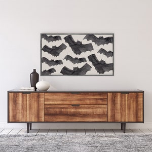 May include: A framed print of a black and white watercolor illustration of bats flying against a white background. The print is hanging above a wooden dresser with two drawers.