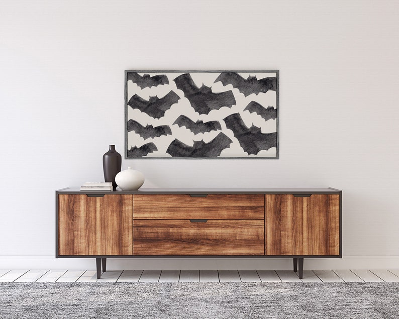 May include: A framed print of a black and white watercolor illustration of bats flying against a white background. The print is hanging above a wooden dresser with two drawers.