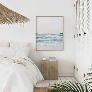 Peut inclure: Une chambre &agrave; coucher blanche avec un lit, une table de chevet en bois et une impression encadr&eacute;e d'une sc&egrave;ne d'oc&eacute;an bleu. Un luminaire de plafond tiss&eacute; est suspendu au-dessus du lit.