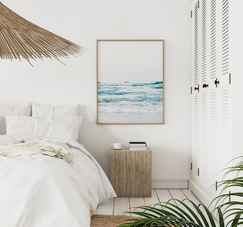 Peut inclure: Une chambre &agrave; coucher blanche avec un lit, une table de chevet en bois et une impression encadr&eacute;e d'une sc&egrave;ne d'oc&eacute;an bleu. Un luminaire de plafond tiss&eacute; est suspendu au-dessus du lit.