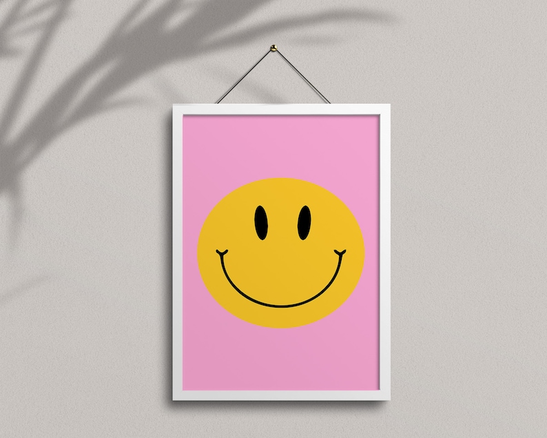 May include: A white framed print with a pink background and a yellow smiley face with black eyes and a black outline.