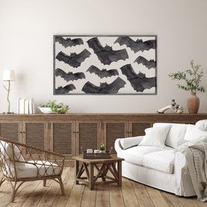 May include: A white living room with a wooden cabinet, a white couch, a wicker chair, and a coffee table. A framed print of black bats on a white background hangs on the wall.
