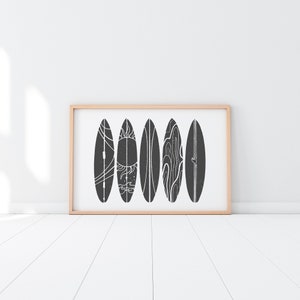 May include: A framed print of six black and white surfboards with different designs. The surfboards are arranged in a row against a white background.