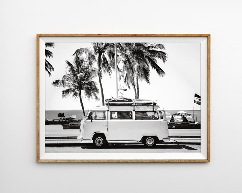 May include: Black and white photograph of a vintage white van parked on a street with palm trees in the background. The van has a surfboard and other luggage strapped to the roof.