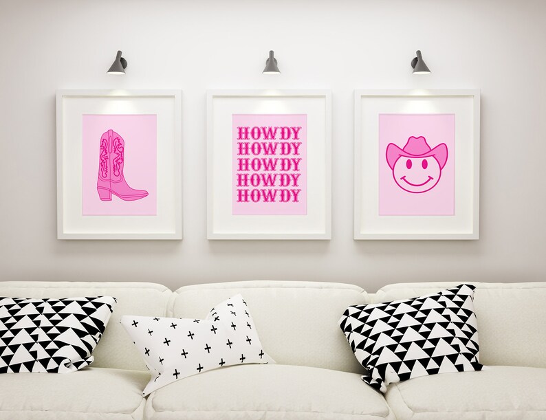 May include: Three framed prints with pink backgrounds and pink outlines. The left print features a pink cowboy boot. The middle print has the word "HOWDY" repeated five times. The right print features a pink smiley face wearing a cowboy hat.
