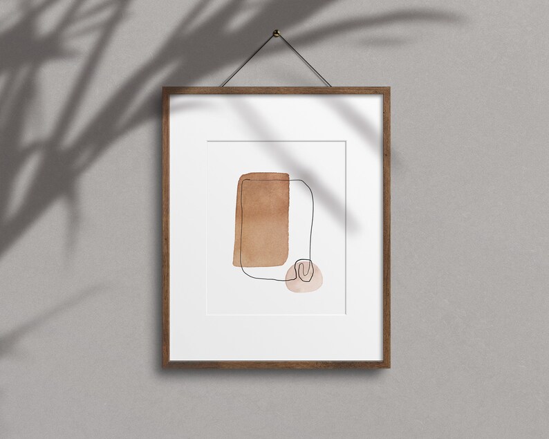 Op de afbeelding: Een ingelijst abstract kunstprint met een bruine aquarel vorm en een dunne zwarte lijn tekening. De print is op een witte achtergrond en heeft een houten lijst.